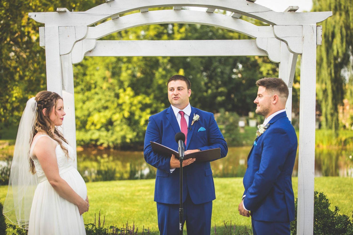 White decorative pergola frames an intimate outdoor wedding ceremony.