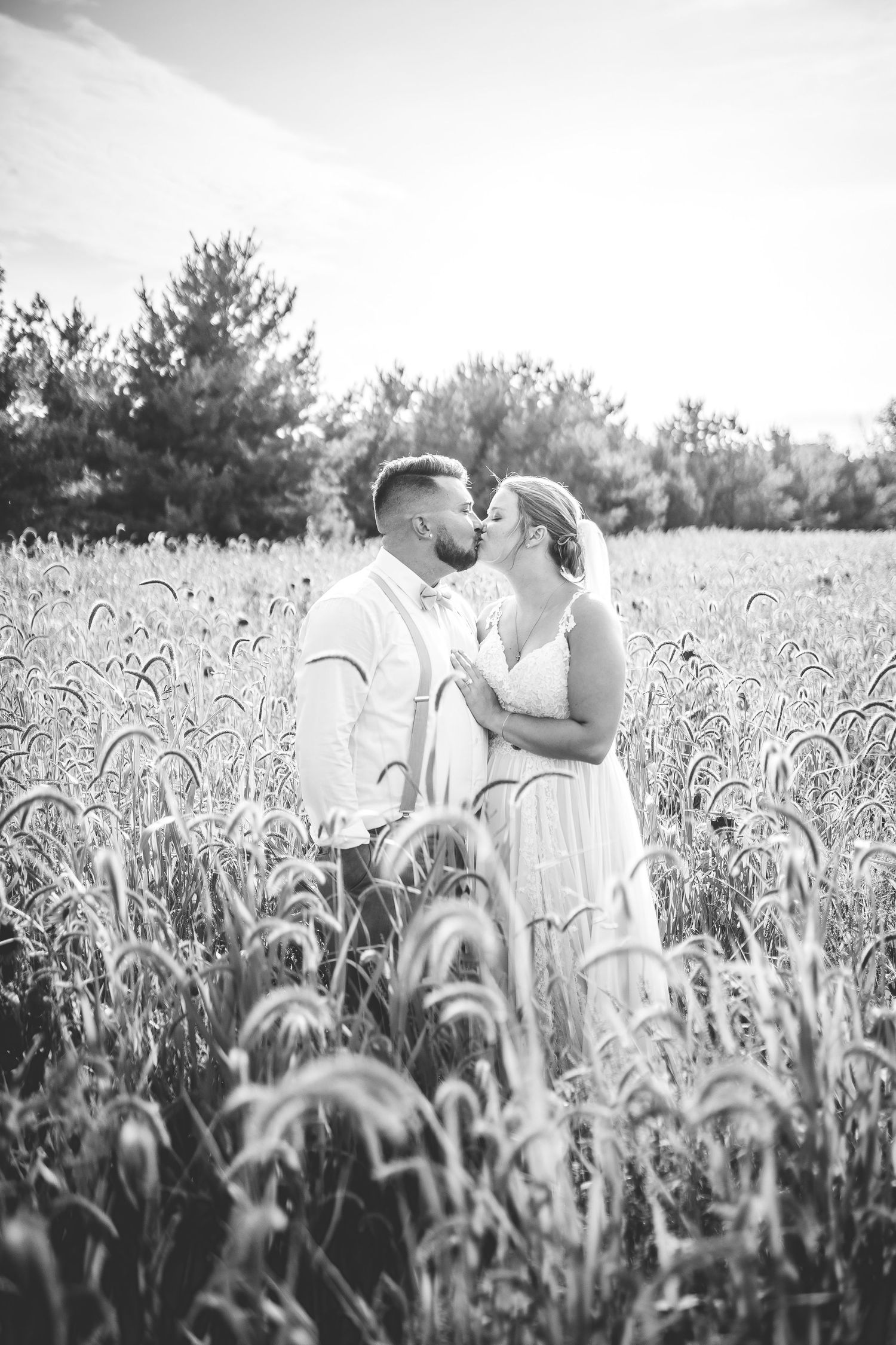 Black and white portrait of couple embracing in tall grass field.