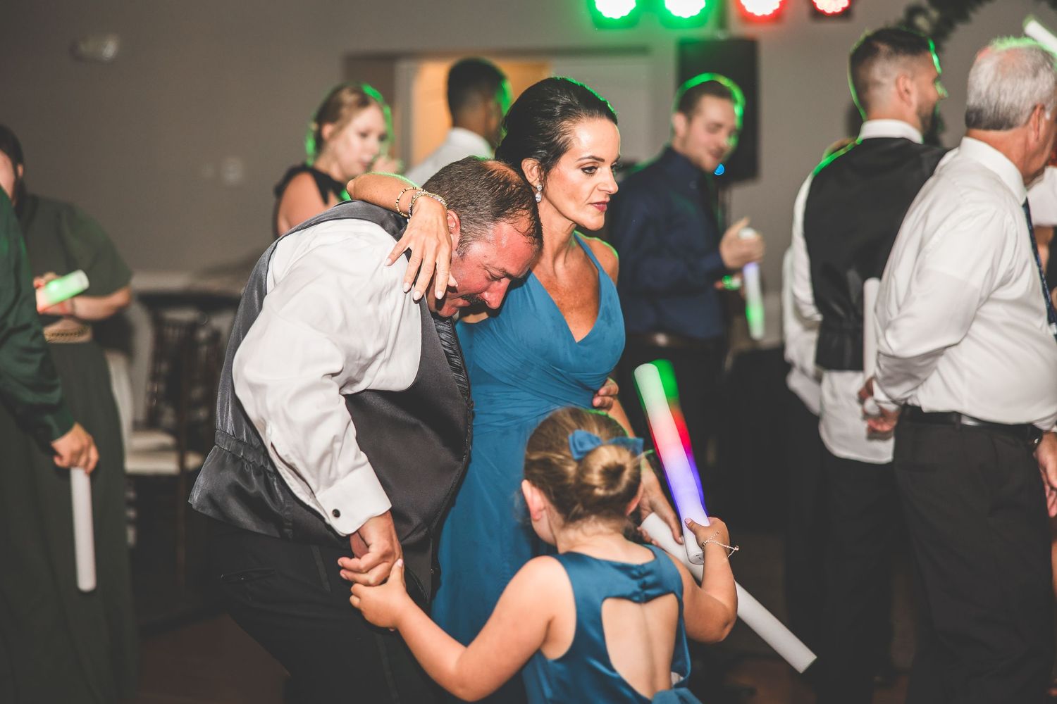 Wedding reception guests dancing and celebrating with glow sticks on a dark dance floor.