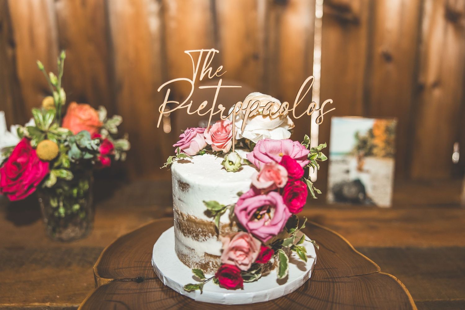 Wedding cake display with fresh pink roses and rustic wooden backdrop.