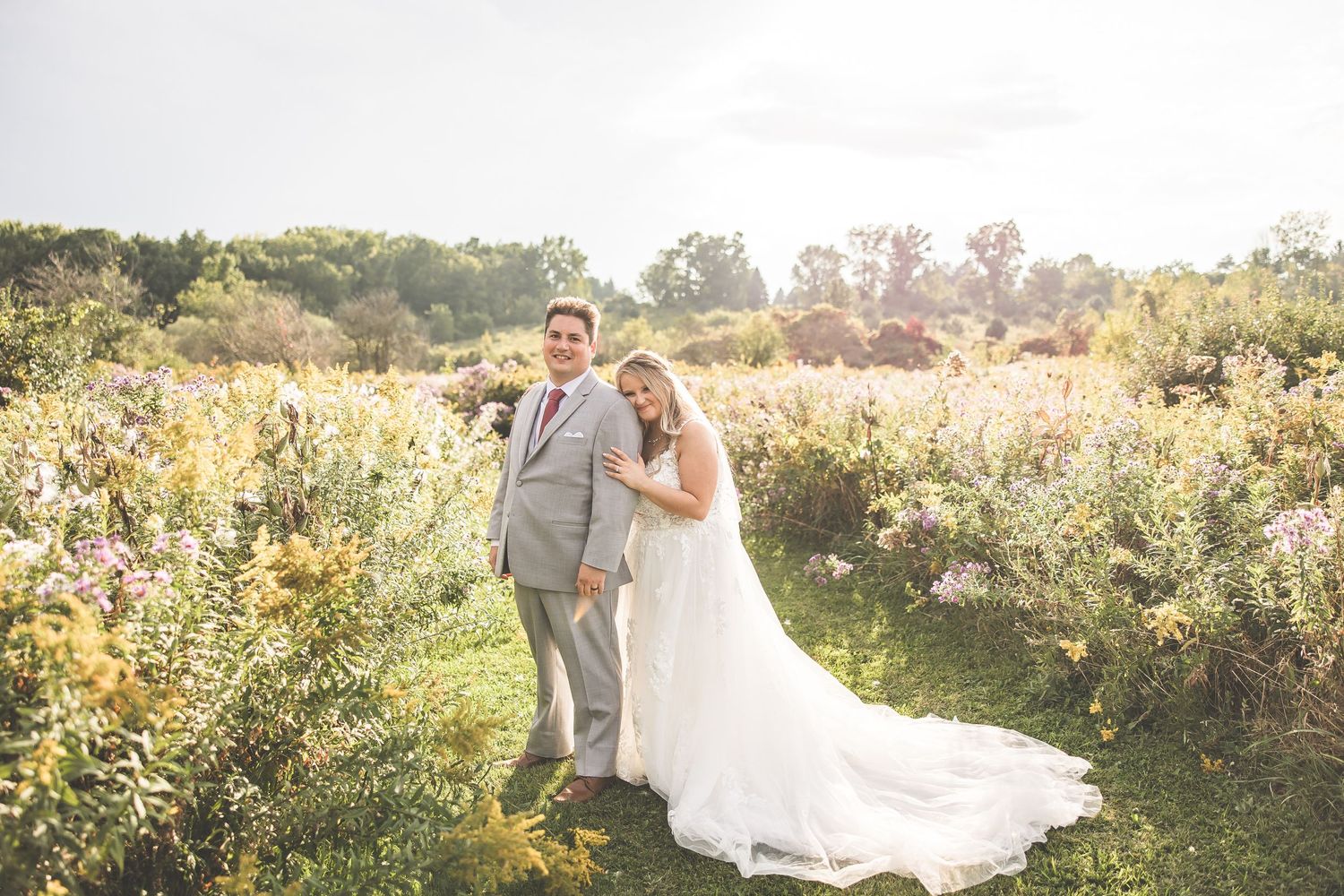 Couple poses in a romantic outdoor garden setting with lush greenery and natural sunlight.