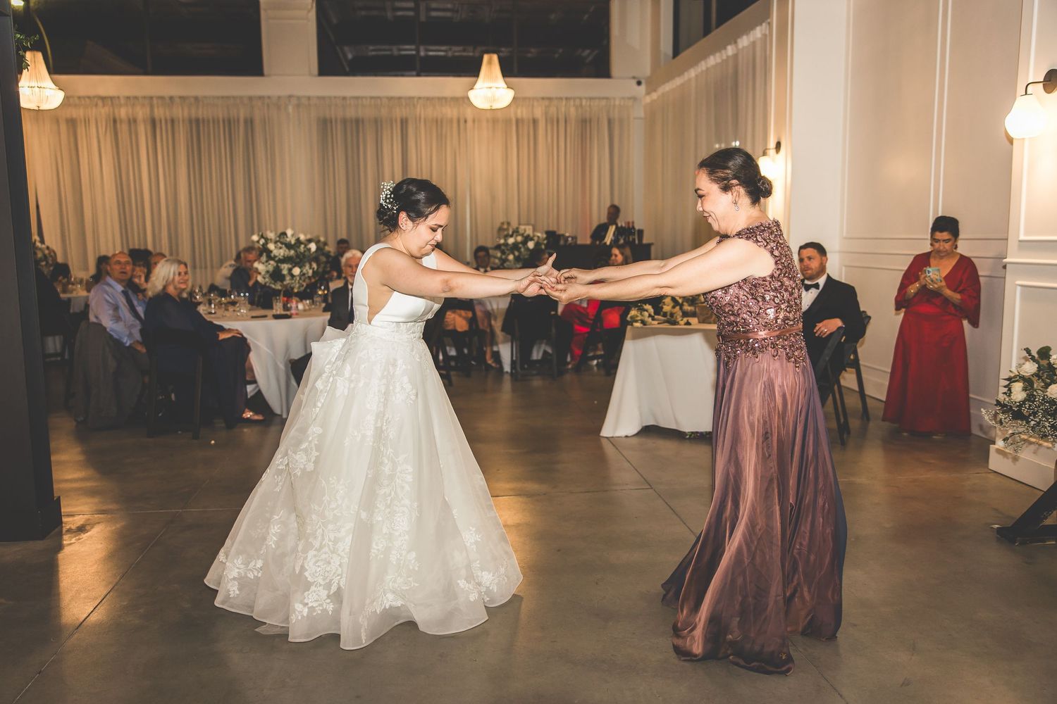 Couples dancing together at a formal wedding reception in an elegant venue with pendant lighting.