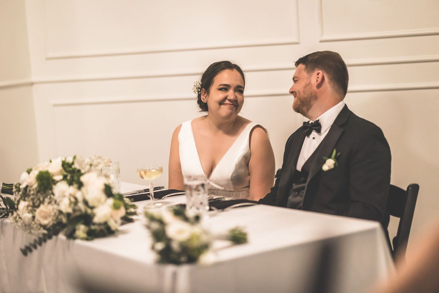 Couple shares an intimate moment at their wedding reception table with white decor.