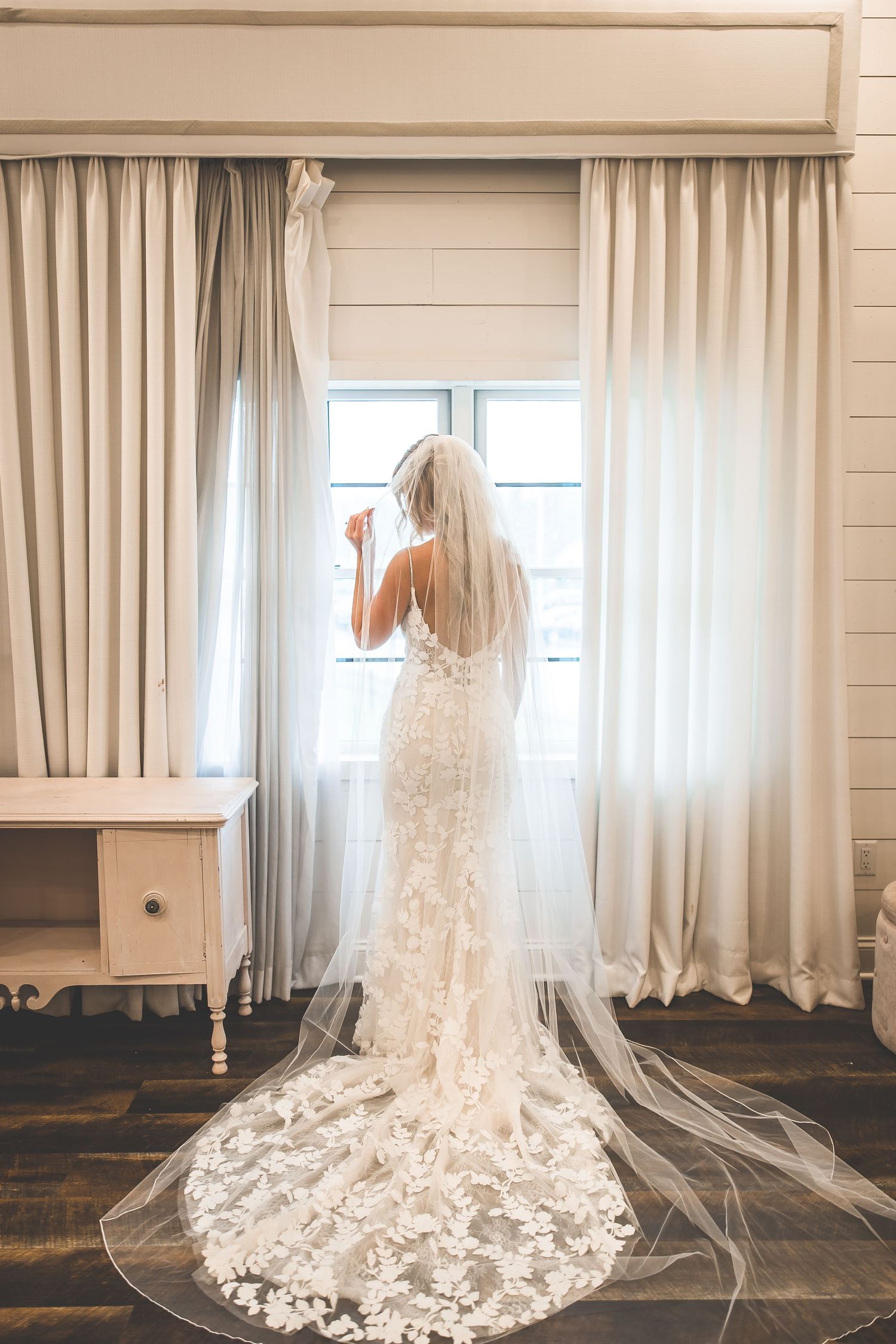 A stunning lace wedding dress with cathedral veil displayed in a bright white room.