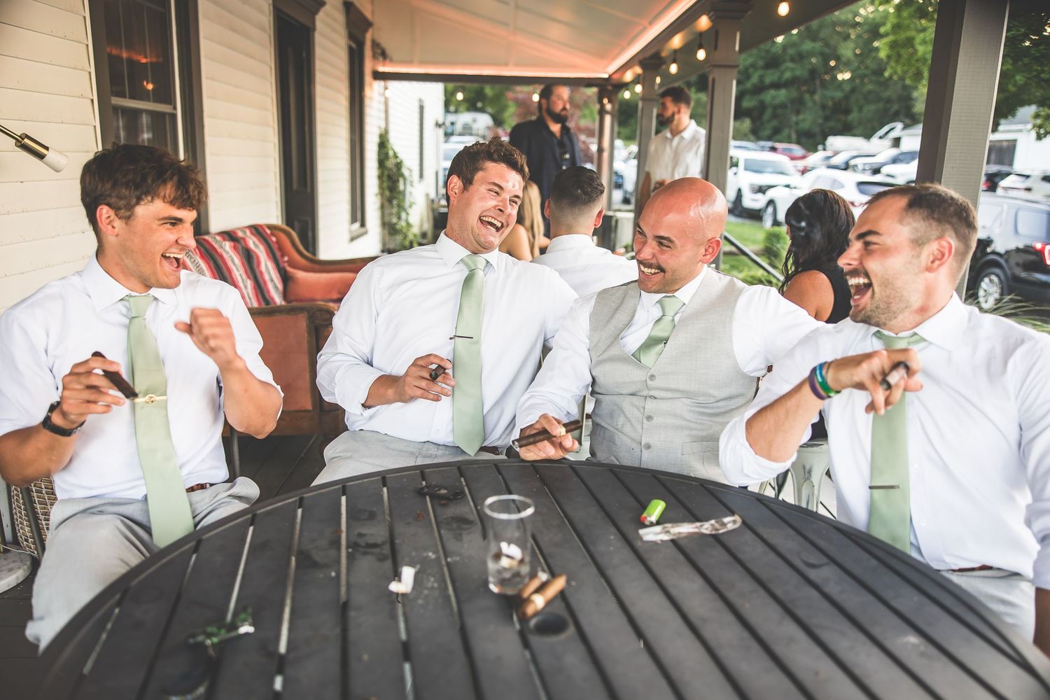 Groomsmen in white shirts and mint green ties enjoying drinks at outdoor bar.