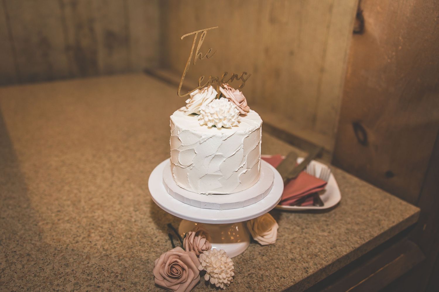 An elegant white wedding cake displayed at a rustic indoor reception venue.
