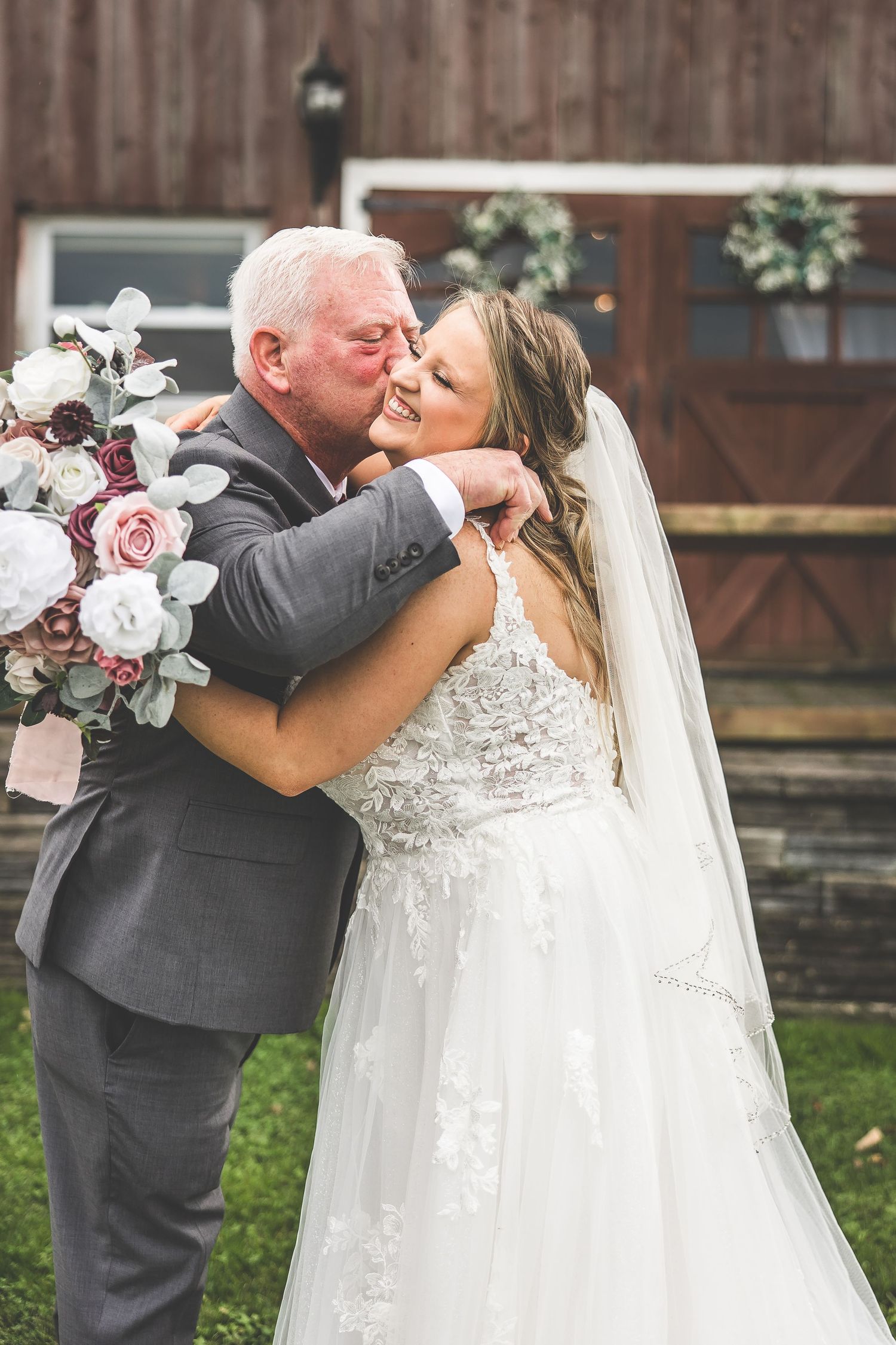 Emotional embrace captured during wedding celebration in front of rustic barn backdrop.