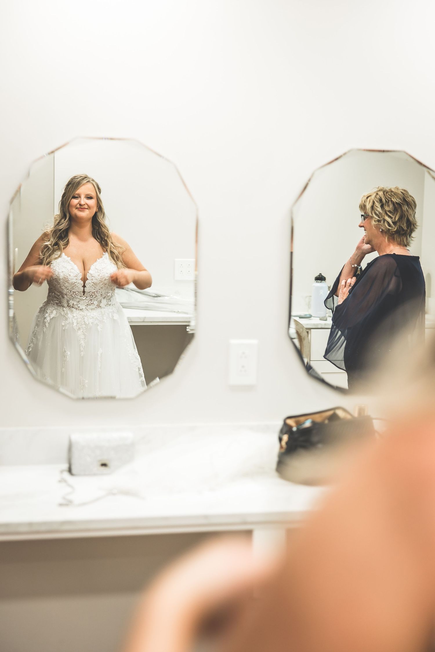 Bride admires her wedding dress reflection in a bathroom mirror.
