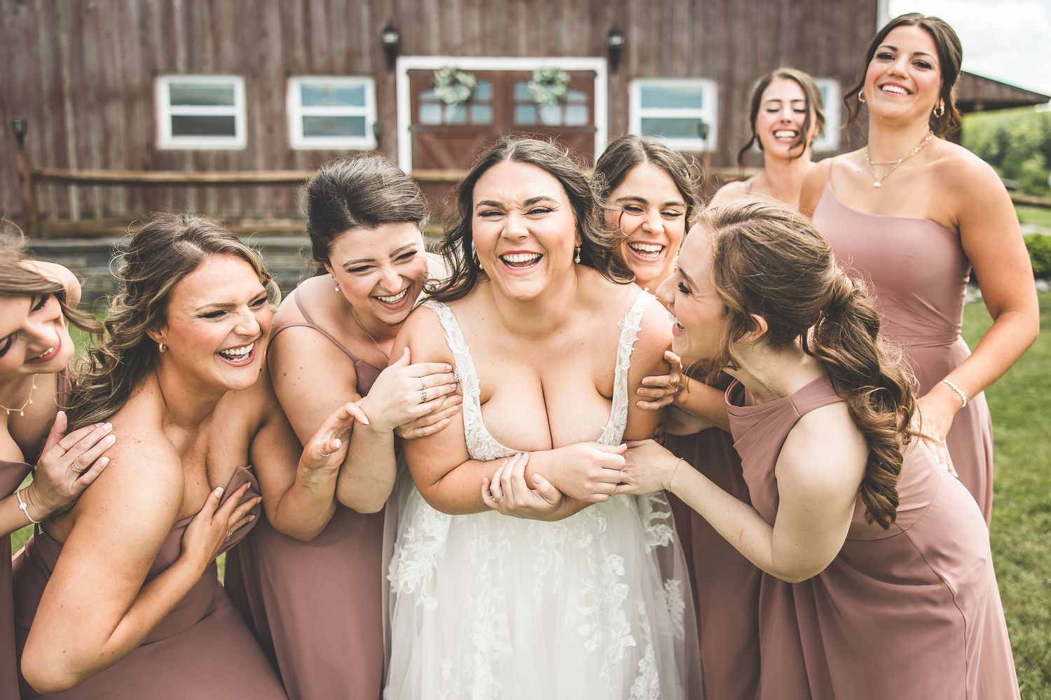 Wedding party sharing candid laughing moments in front of rustic barn setting.
