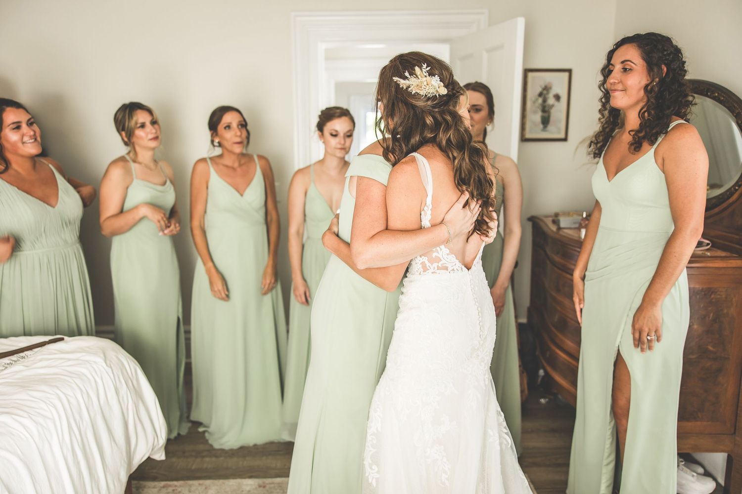 Wedding party wearing sage green bridesmaid dresses pose together in a line.
