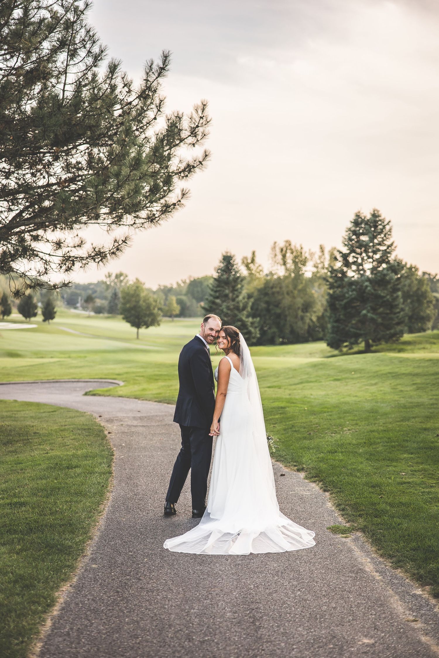 Wedding couple photographed from behind walking along curved path on golf course.