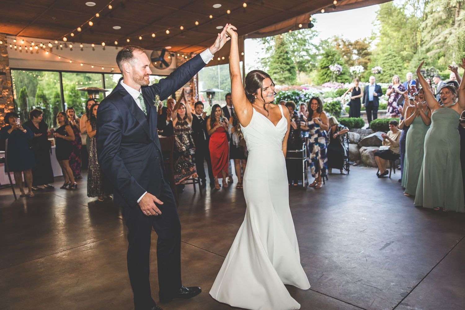 Wedding reception dance floor filled with guests under string lights at an indoor venue.
