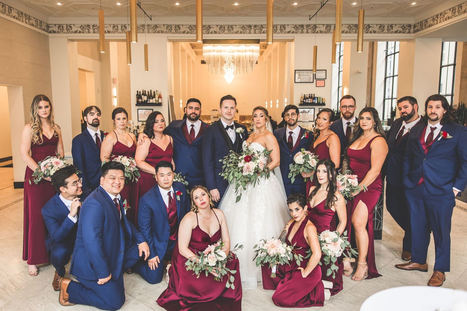 Wedding party members pose casually in elegant venue with ornate ceiling details.