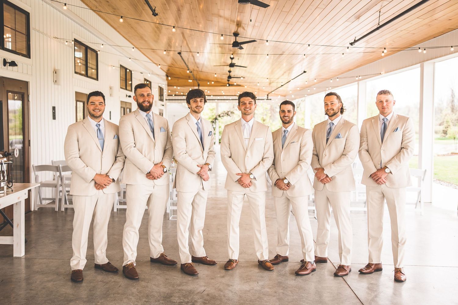 Groomsmen in matching cream suits and blue ties pose together in modern venue.