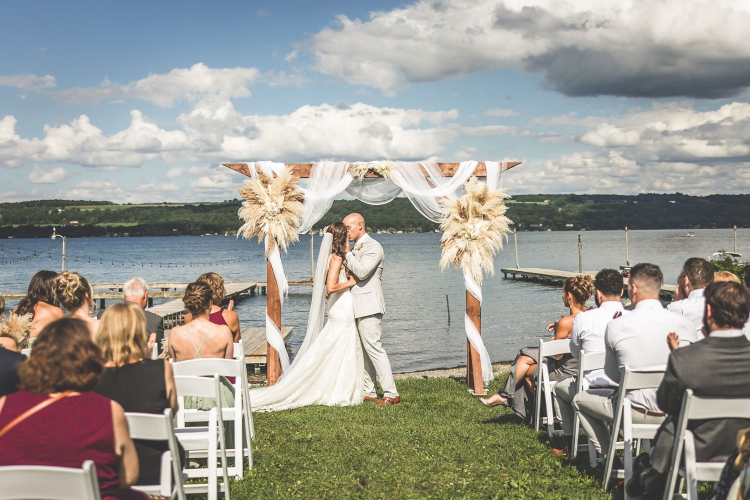 Wedding ceremony setup with white chairs on a grassy lawn overlooking a scenic waterfront view.