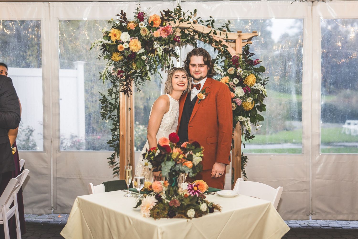 Elegant wedding arch adorned with peach and orange floral arrangements in an outdoor tent setting.