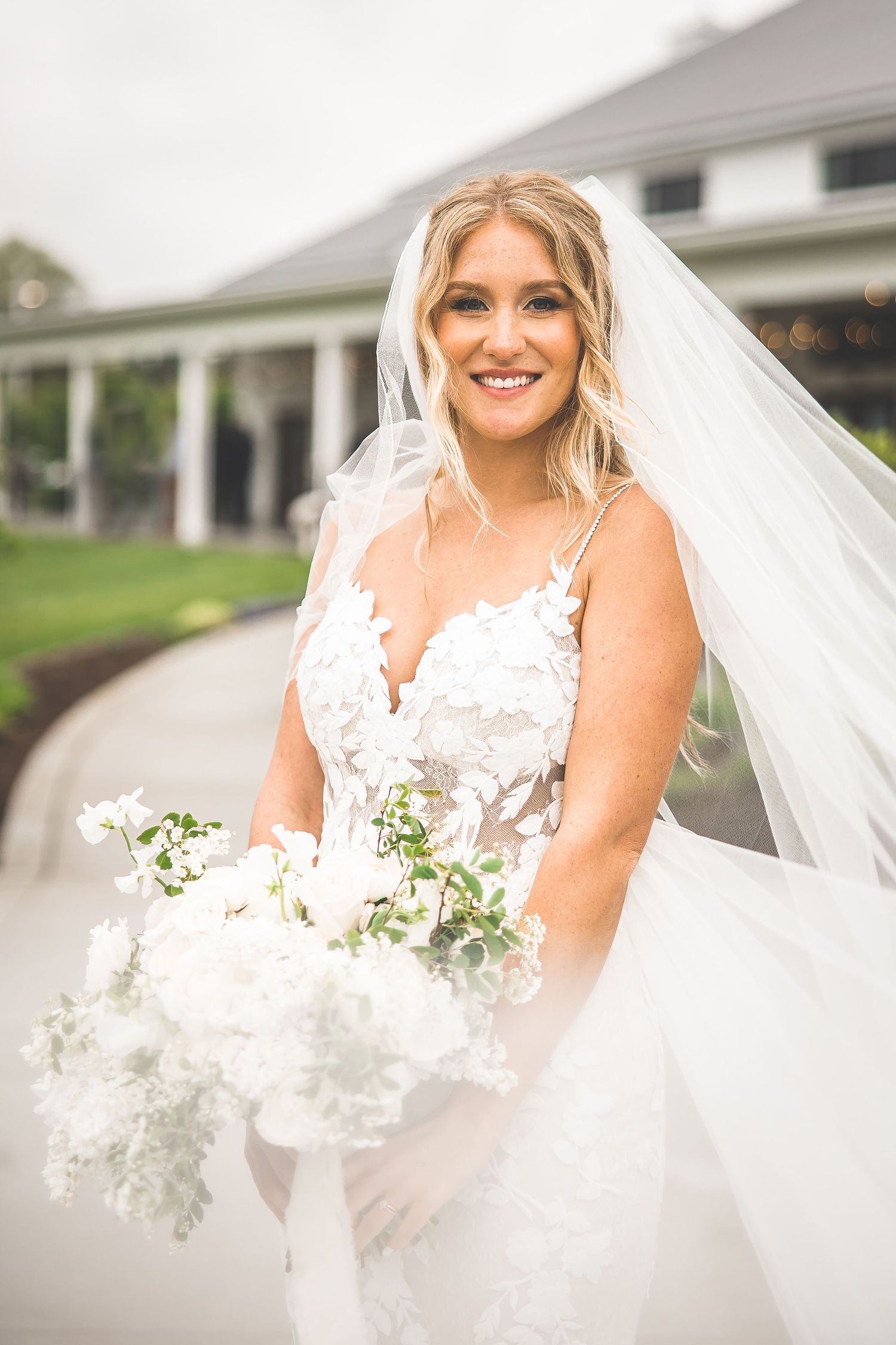 Close-up of bride in white lace gown holding bouquet against venue backdrop.