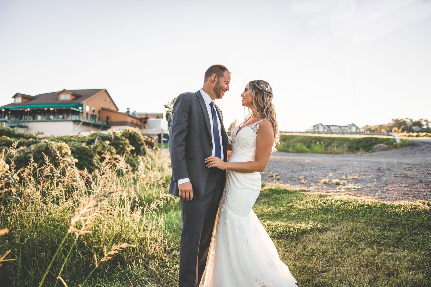 Wedding couple posing in golden sunlight on grassy field near waterfront.