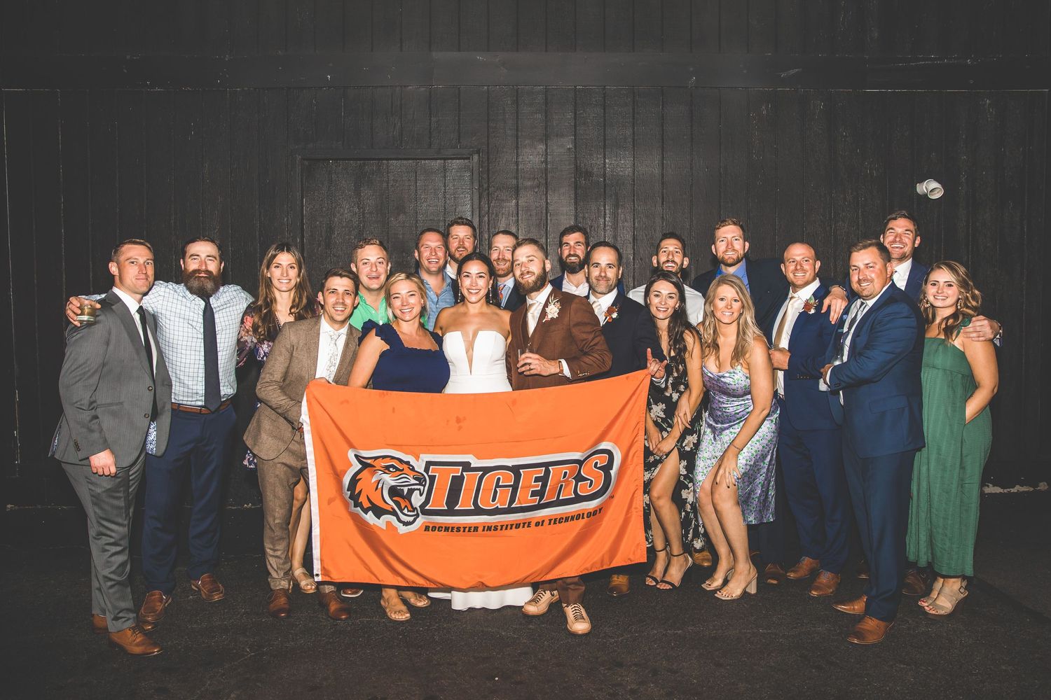 Wedding party group photo with guests holding an orange Tigers banner.