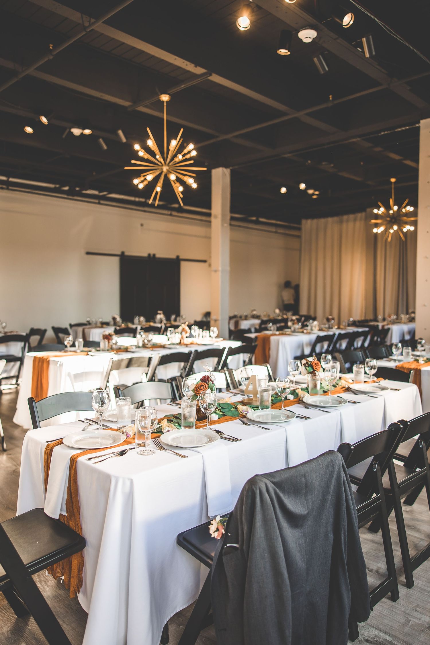 Modern wedding reception venue with starburst chandeliers and long tables set with white linens.