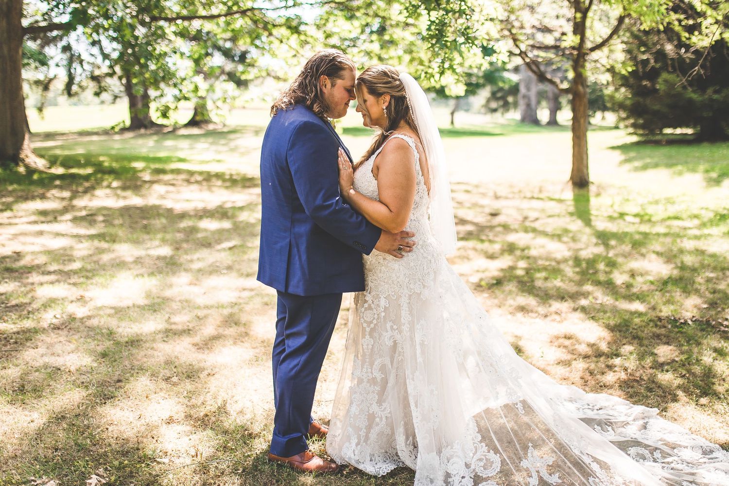 Wedding couple embracing in a sun-dappled garden setting.