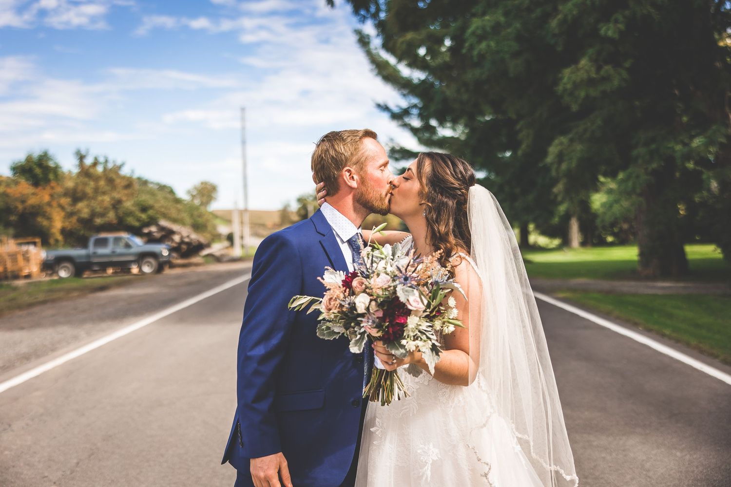 Wedding couple walking and embracing on a sunny road with trees in the background.