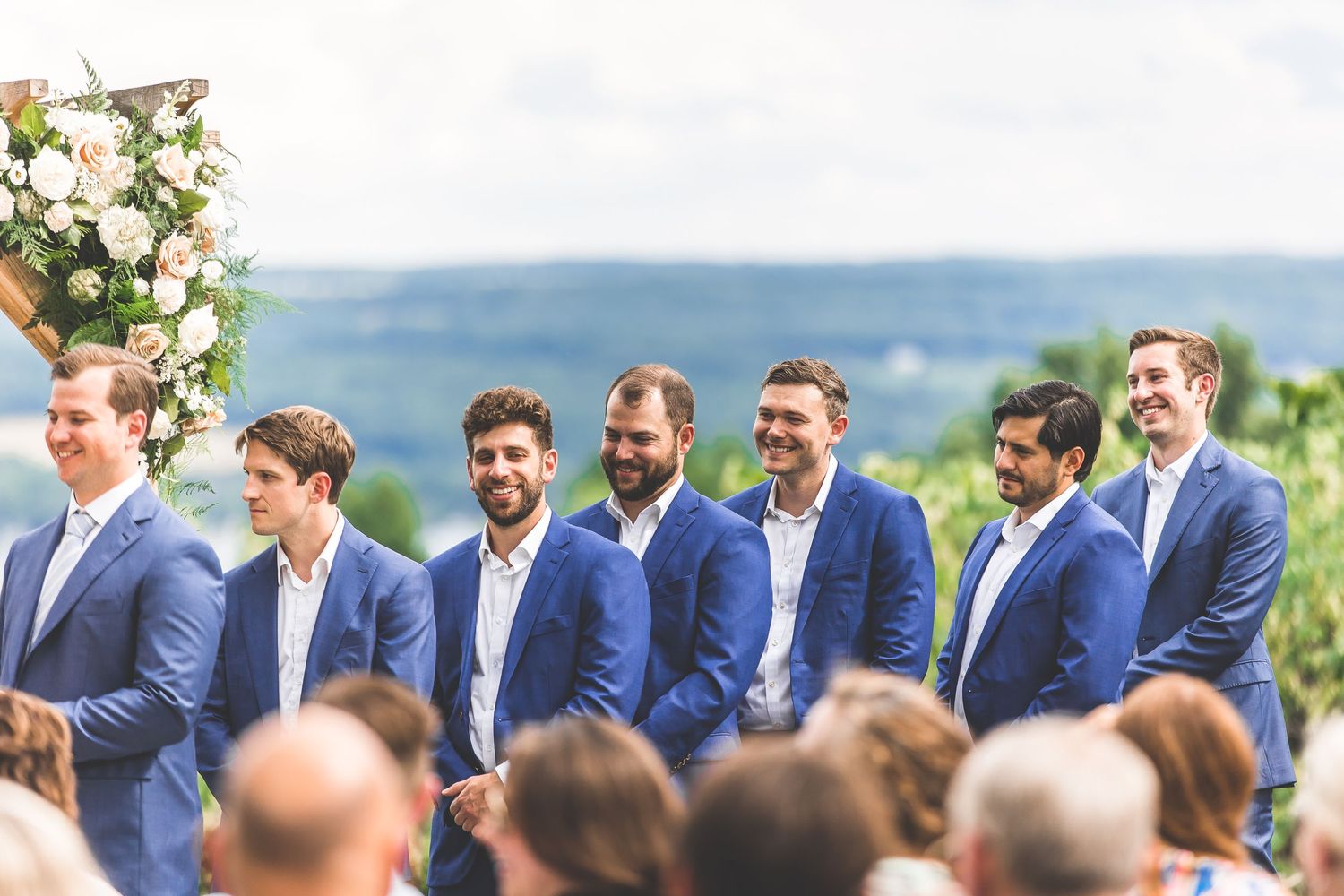 Wedding party members in navy blue suits standing in line during outdoor ceremony.