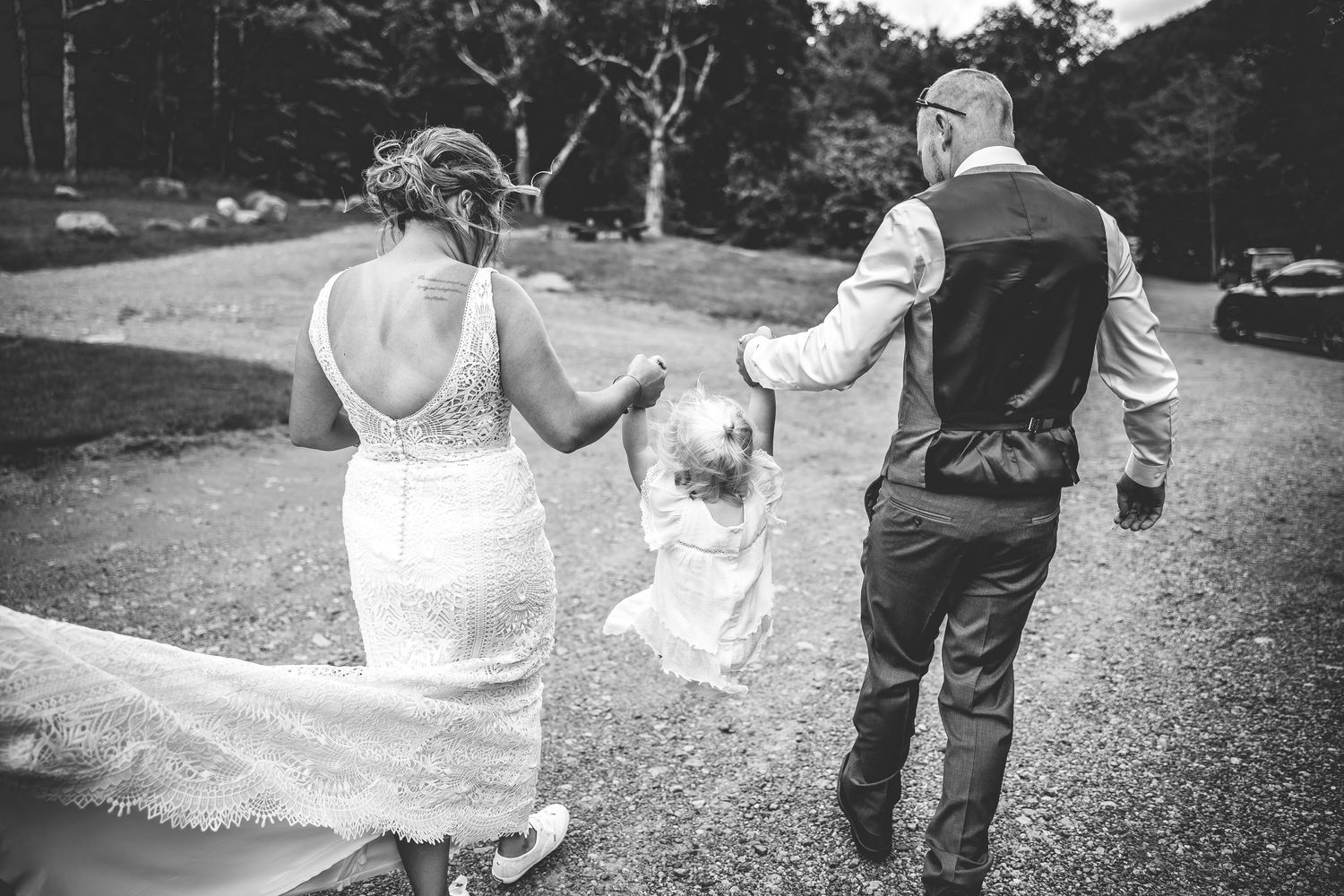 Wedding dress train trails behind couple walking along lakeside path.