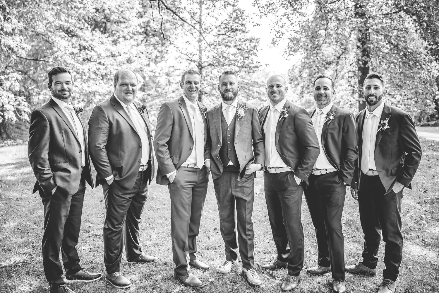 Groomsmen lineup photographed in black and white under trees.