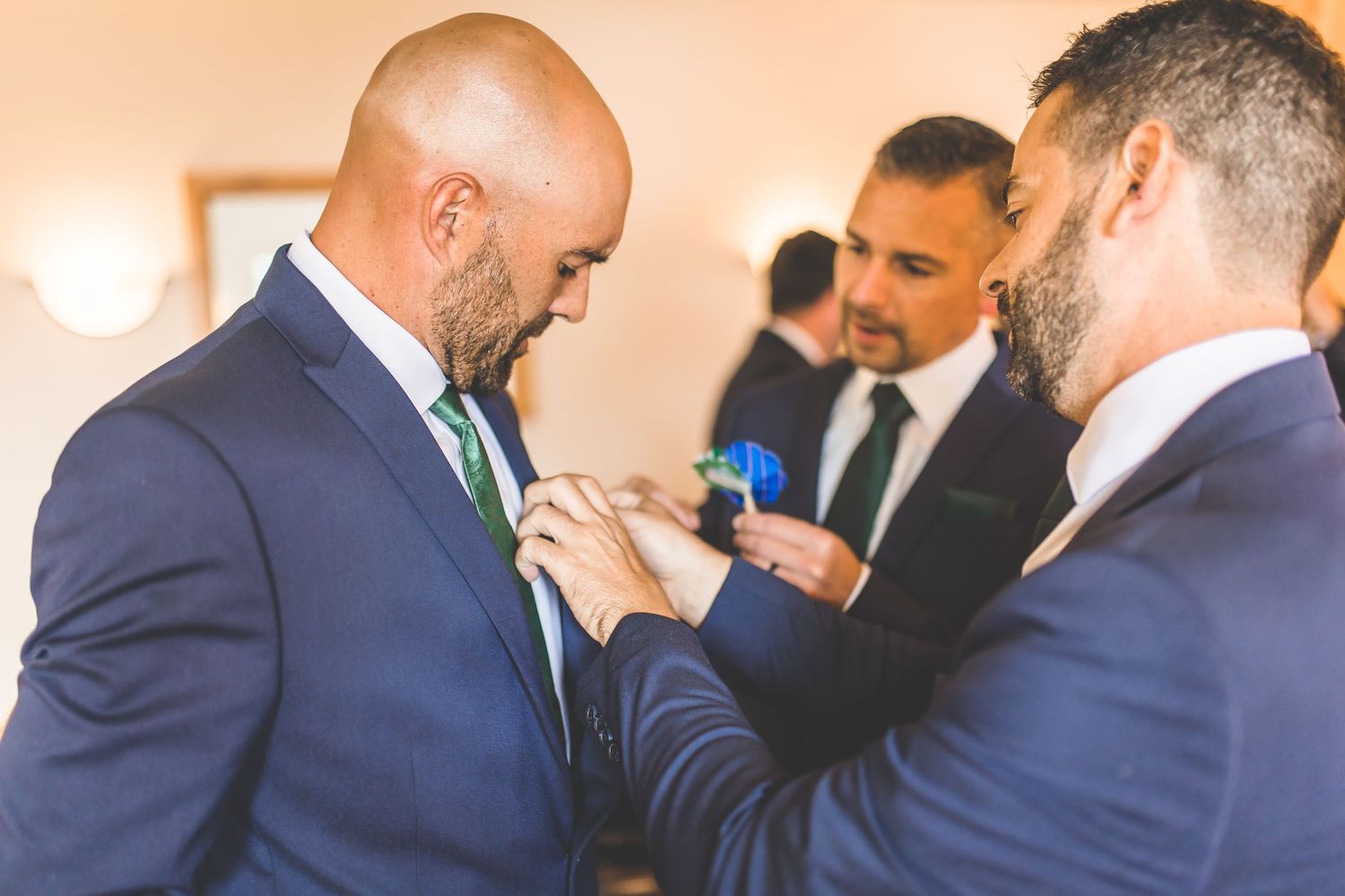 Groomsmen in matching navy suits and green ties share candid moments.