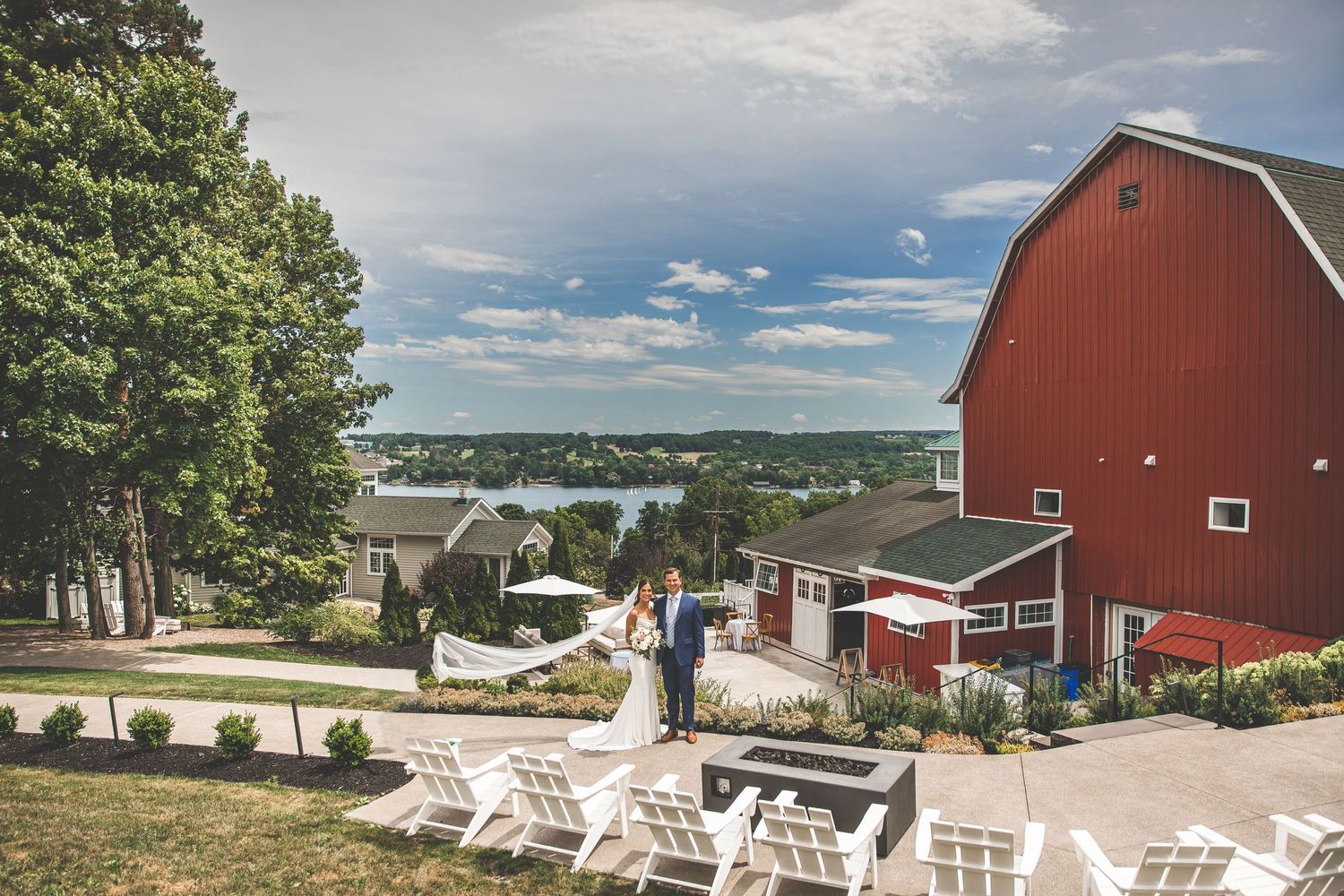 Scenic view of a rustic red barn wedding venue with white picnic tables and countryside views.
