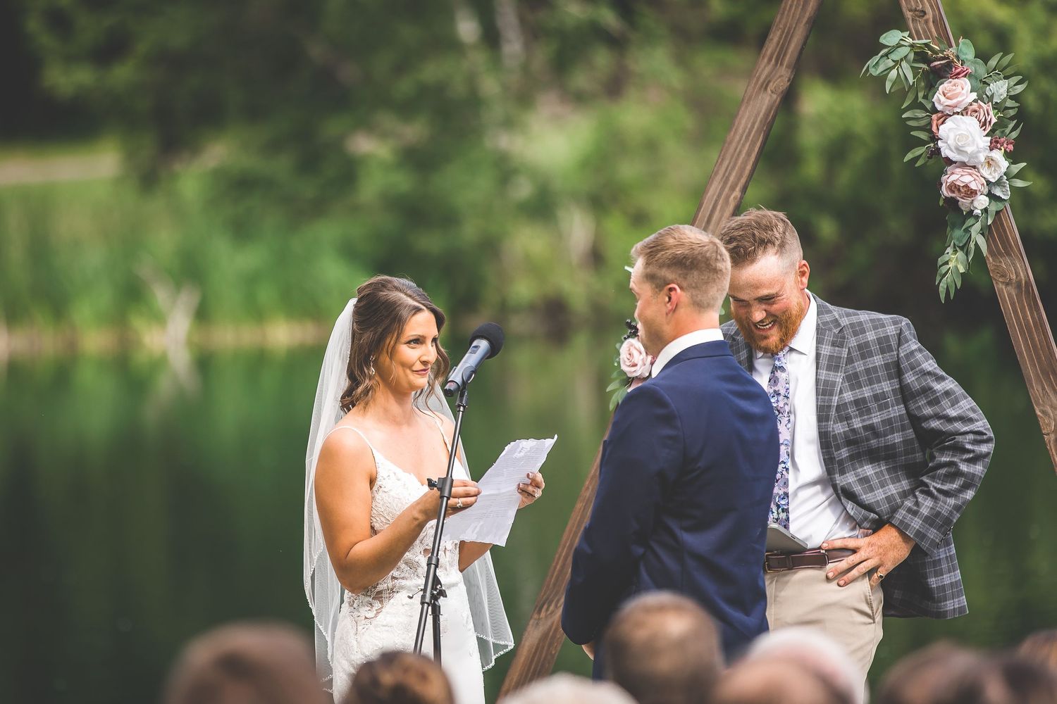 Close-up view of wedding ceremony moments with wooden triangle arch and lake backdrop.
