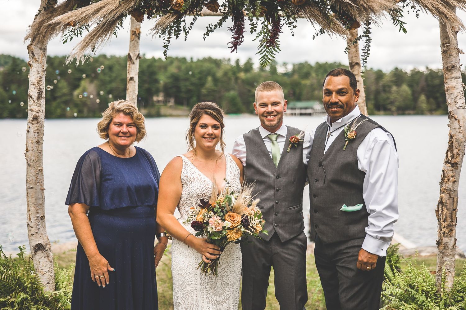 Wedding party gathers for photos under a handcrafted birch arch by the waterfront.