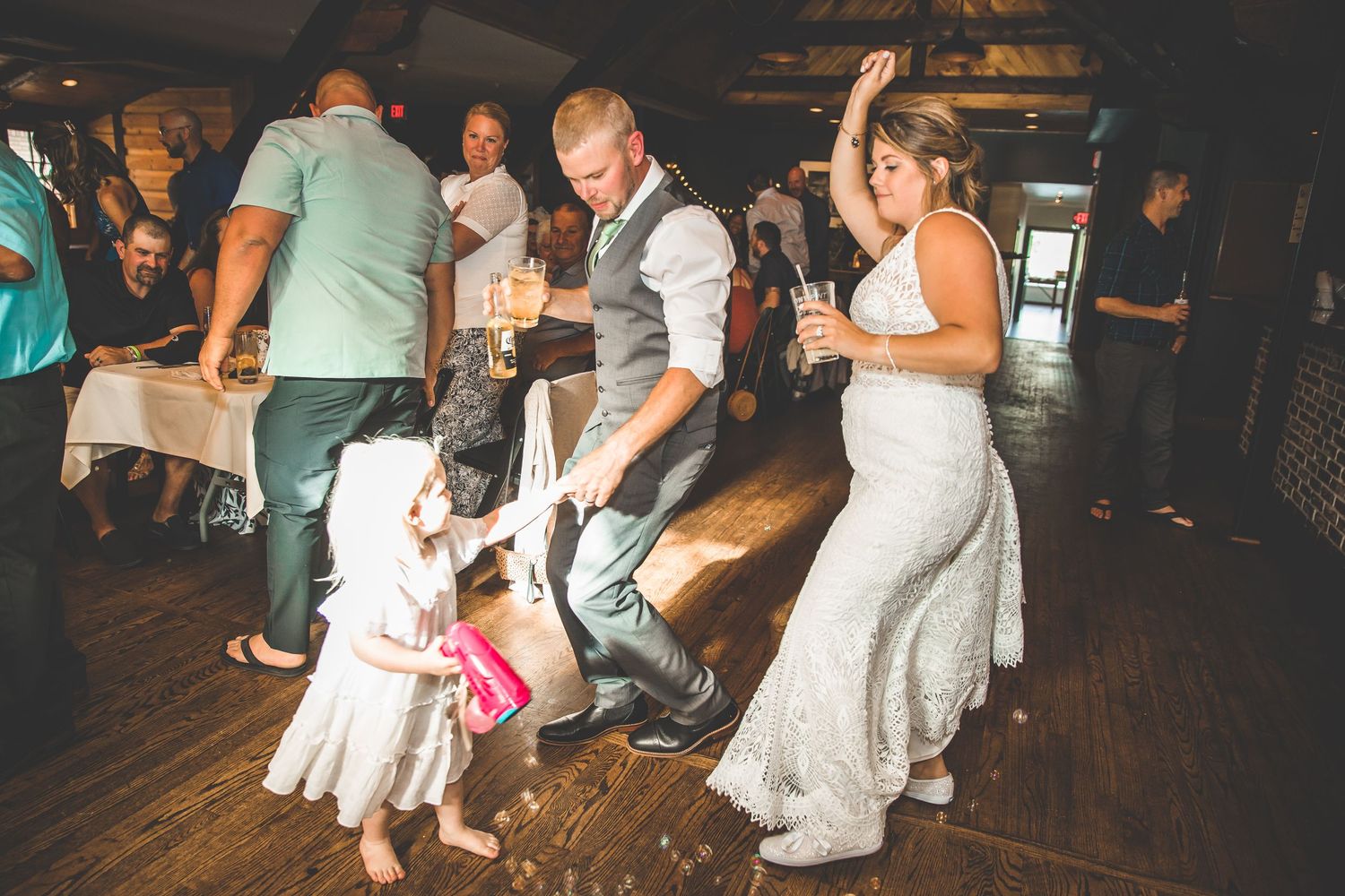 Wedding reception dance floor with guests celebrating in a dimly lit rustic venue.
