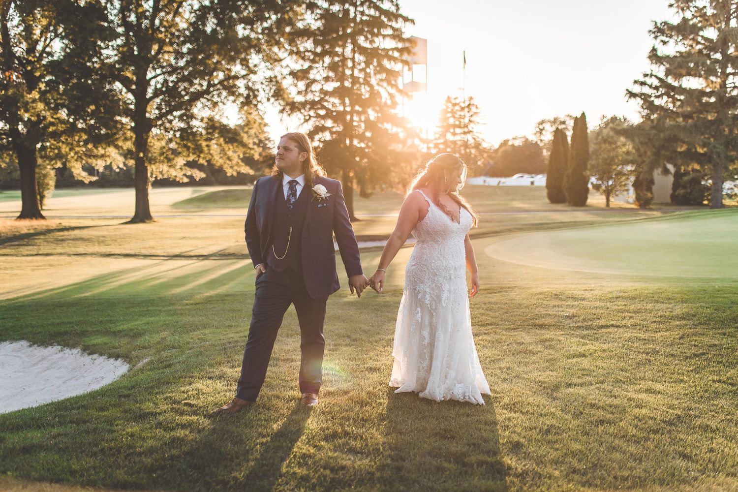 Newlyweds walking together on golf course during sunset.