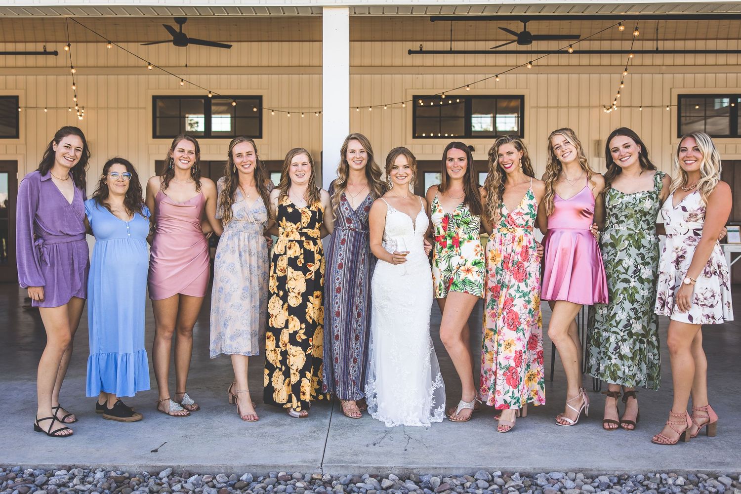 Wedding party group photo with colorful dresses against a neutral building exterior.