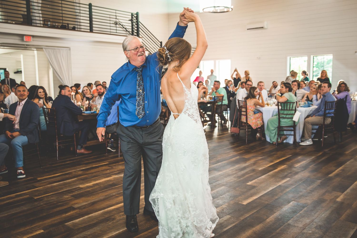 A couple shares their first dance at a wedding reception as guests look on in a bright indoor venue.