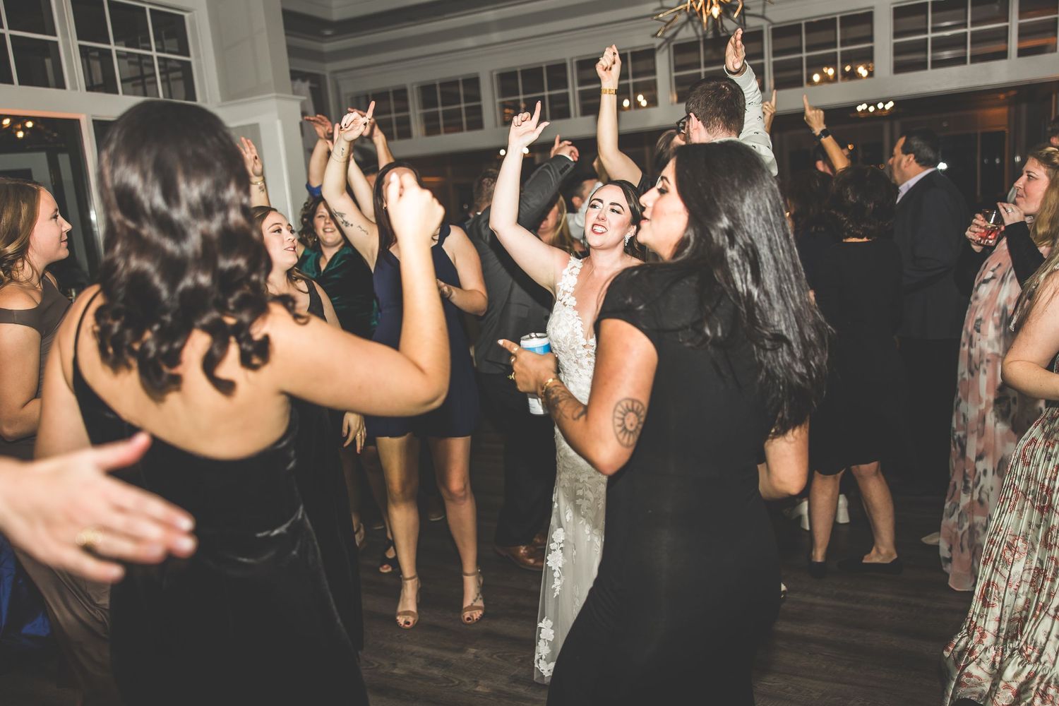 Wedding guests dancing and celebrating on a lively dance floor at an indoor reception venue.