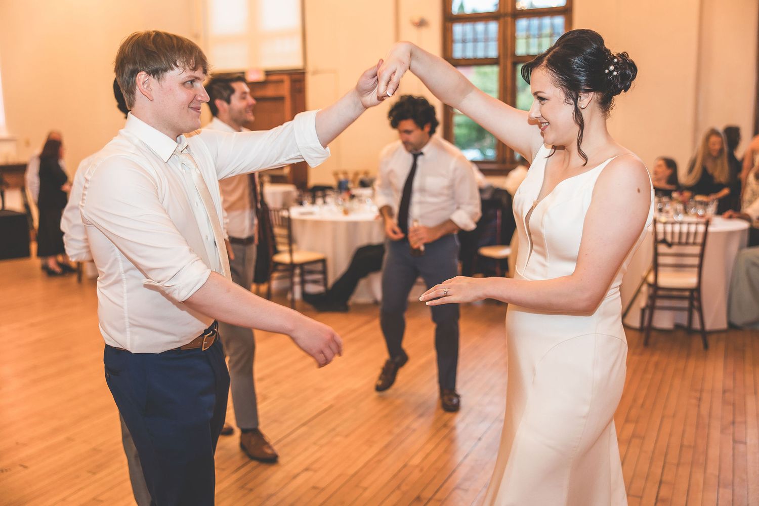 Couples dancing together on a wooden dance floor at an elegant wedding reception venue.