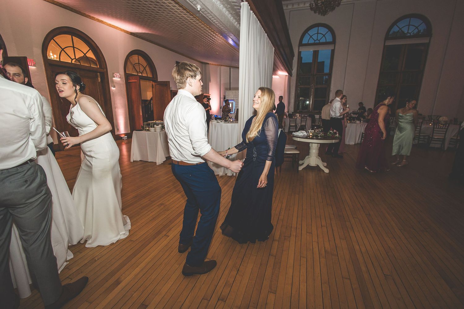 Guests enjoying themselves at an elegant wedding reception with hardwood floors and ambient lighting.
