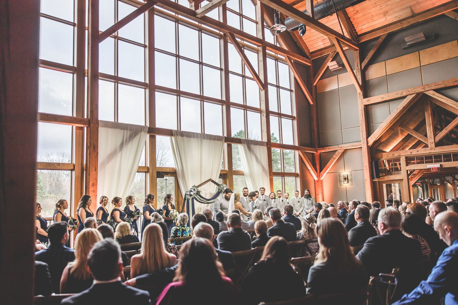 Wide-angle view of wedding guests seated in a modern rustic venue with natural lighting.