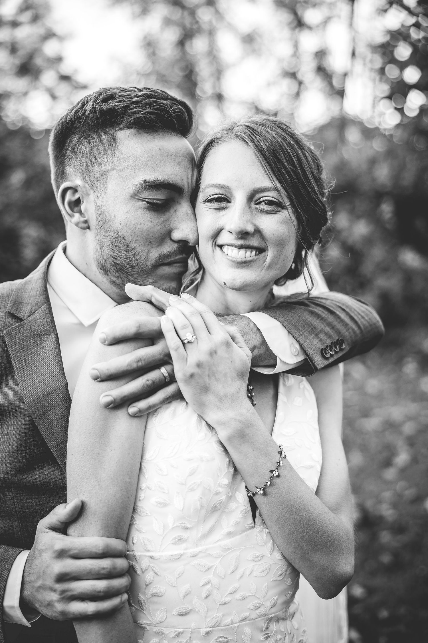 Black and white intimate portrait of newlyweds embracing while showing wedding ring.