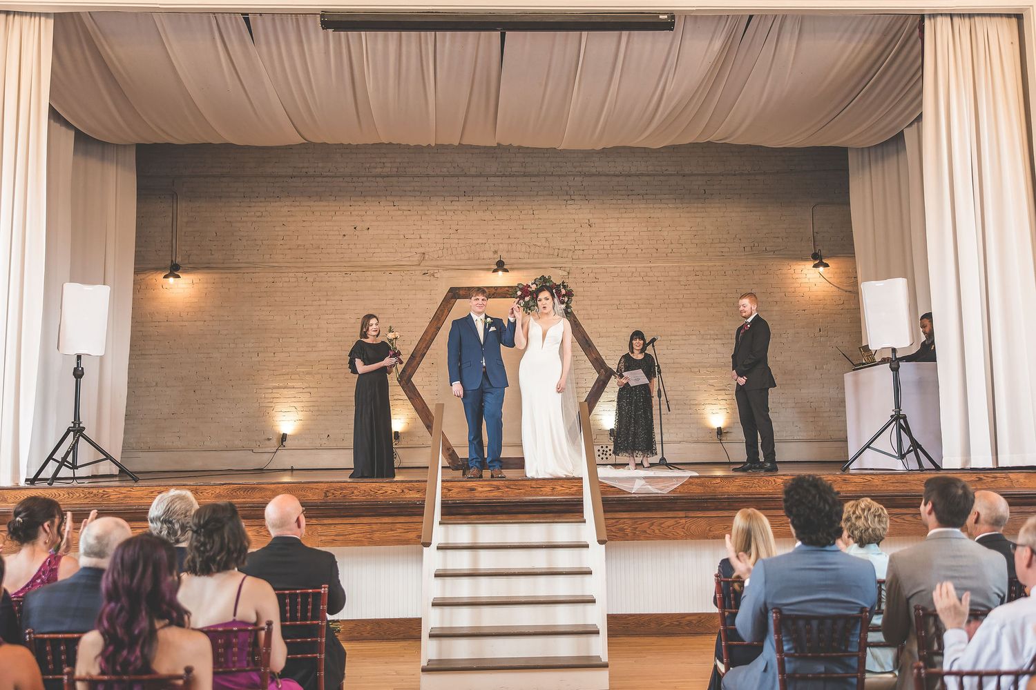 Wide view of wedding ceremony venue with guests seated in rows facing decorated altar area.