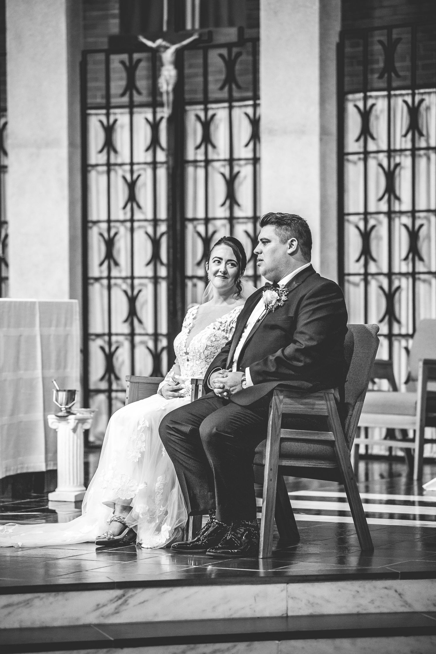 Black and white photo of a couple relaxing on chairs in a church hallway.