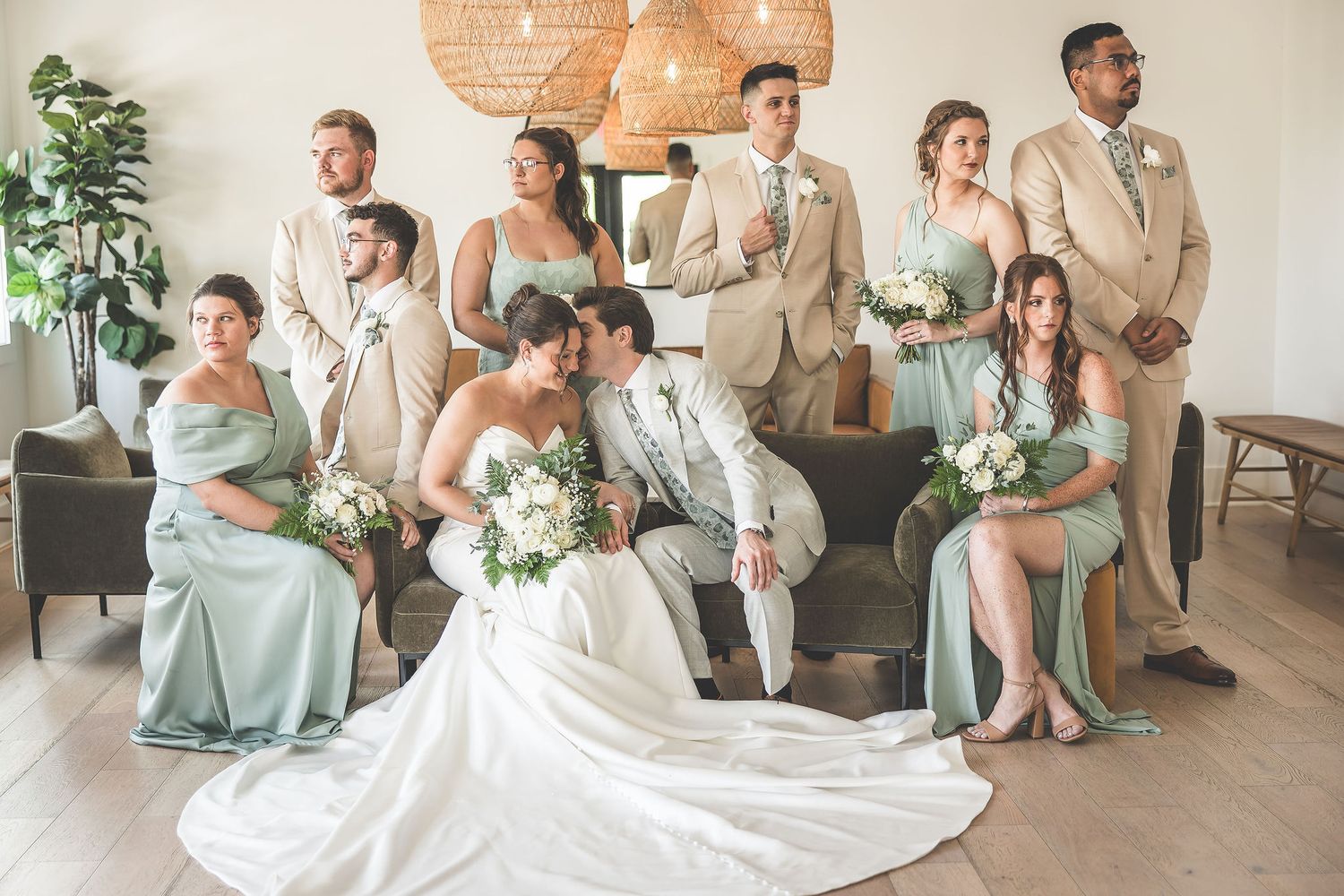 Wedding party poses in modern room with sage bridesmaid dresses and tan suits.