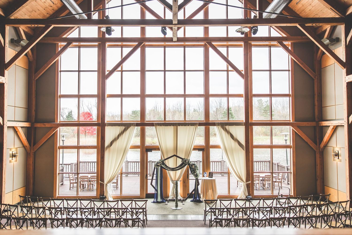 Rustic wooden event venue interior with exposed beams and large windows creating warm natural lighting.