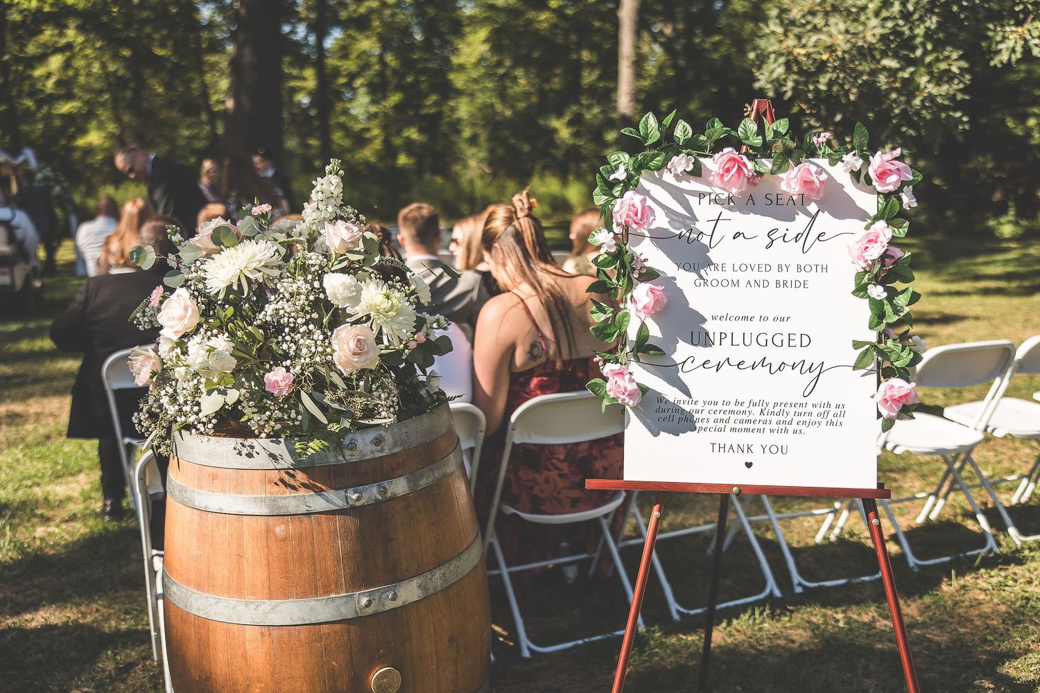 Wedding guests seated in white chairs at an outdoor ceremony with wine barrel decorations.