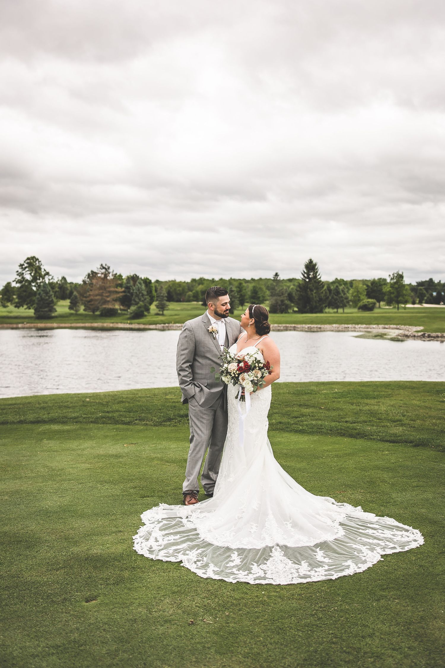 Couple poses for romantic wedding photos on a scenic golf course near a lake.