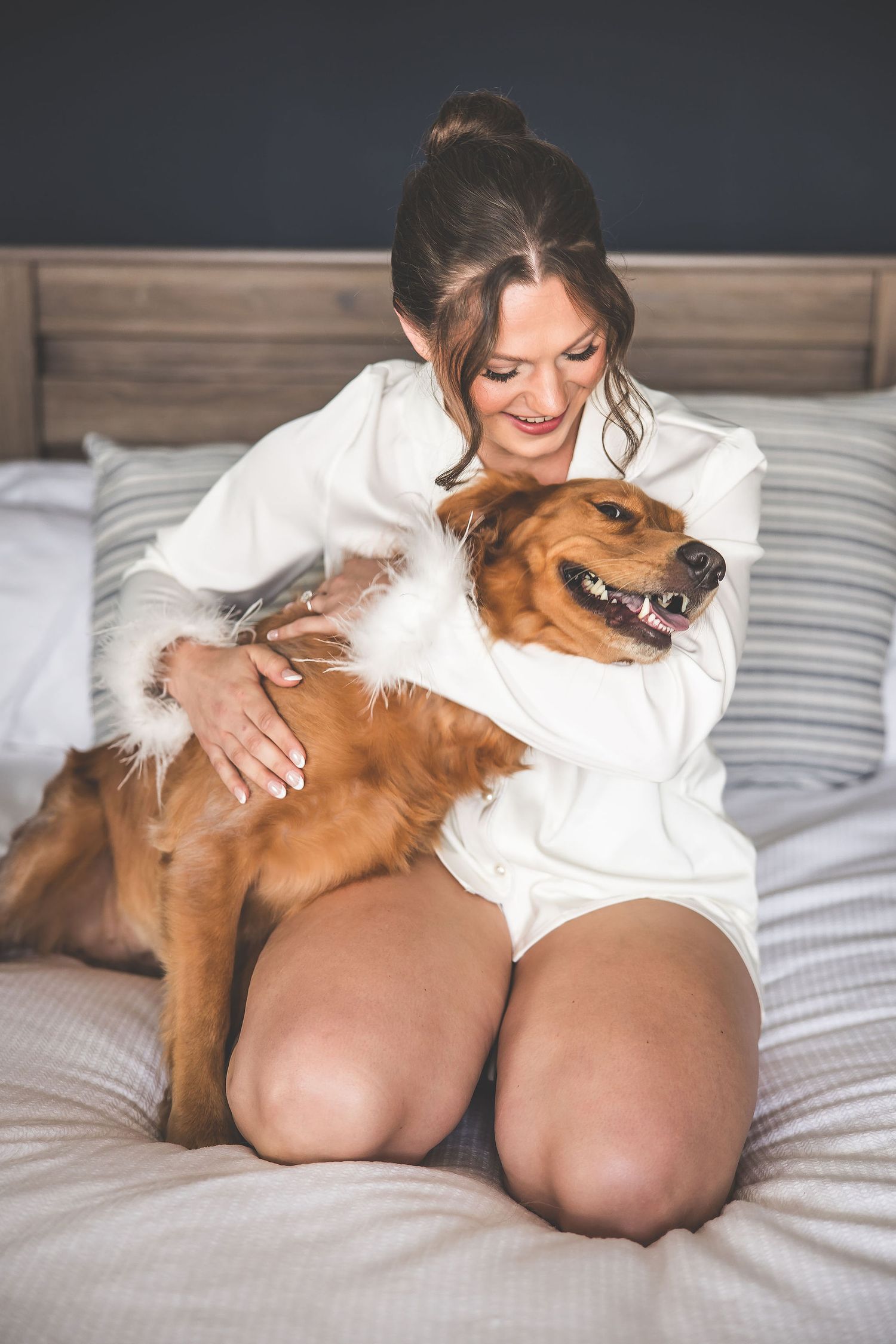 A relaxed moment captured with a smiling golden retriever and someone in white loungewear on a cozy bed.