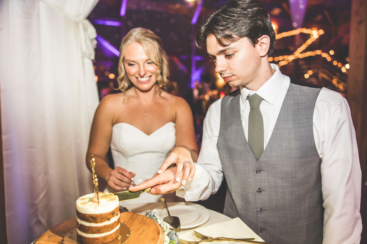 Wedding cake cutting ceremony with a rustic naked layer cake decorated with gold accents.